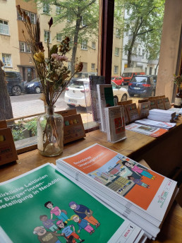 zwei verschiedene Broschüren liegen auf einer Ablage vor einem Fenster