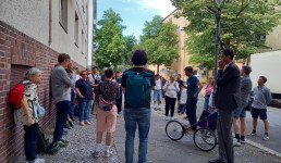 mehrere Personen stehen auf einem Bürgersteig und hören einer anderen Person zu