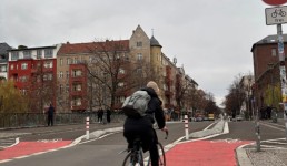 Eine Person fährt auf einer Brücke entlang eines rot markierten Radwegs und im Hintergrund kahle Bäume zu sehen sind