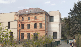 Gebäude mit Anbau und links Äste und Sträucher. Rechts drei Personen 