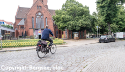 Foto einer Kirche vor der eine Person auf einem Fahrrad über den Platz fährt