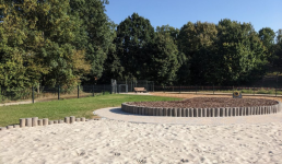 Eingezäunte Fläche, mit Sandfläche und Bäumen im Hintergrund