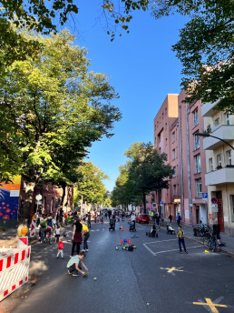 Straße ohne Autos mit spielenden Personen, Häuser und Bäume im Hintergrund