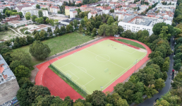 Sportplatz umgeben von Bäumen, Häuser im Hintergrund