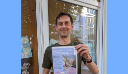 Der Bezirksbürgermeister Neuköllns hält ein Plakat für die Kiez-Tour in die Kamera.